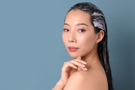 Beautiful Asian woman with hair mask on blue background, closeupの写真素材