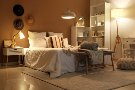 Interior of bedroom with plaids on soft bench and glowing lamps at night