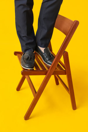 Legs of young man in black stylish shoes on chair against yellow backgroundの写真素材