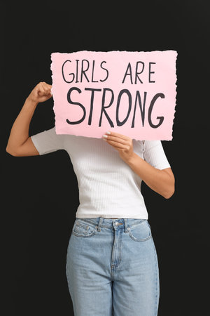 Woman covering face with sign GIRLS ARE STRONG on black background. Feminism conceptの写真素材