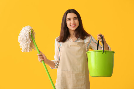 Young woman with floor mop and bucket on yellow backgroundの写真素材
