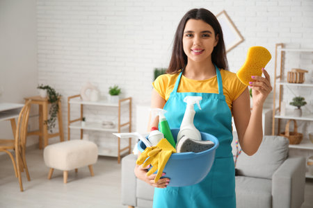 Young woman with sponge and cleaning supplies in living roomの写真素材