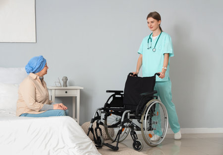 Mature woman after chemotherapy and nurse with wheelchair in bedroom. Stomach cancer conceptの写真素材