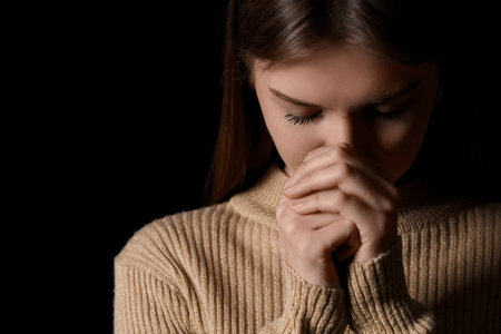 Young woman praying on black background, closeupの写真素材