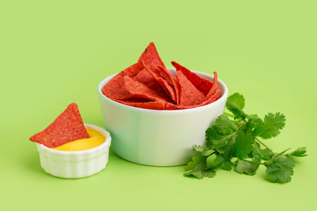 Bowl with red nachos, cheese sauce and parsley on green background