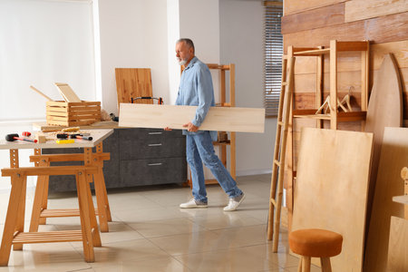 Mature carpenter carrying wooden plank in workshopの写真素材