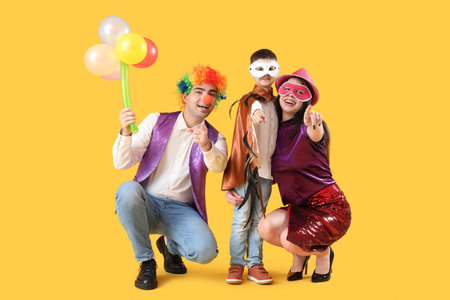 Happy family in costumes and carnival masks on yellow backgroundの写真素材