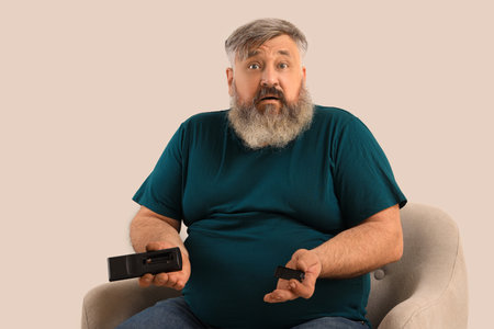 Shocked mature man holding TV remote control with no batteries on light backgroundの写真素材