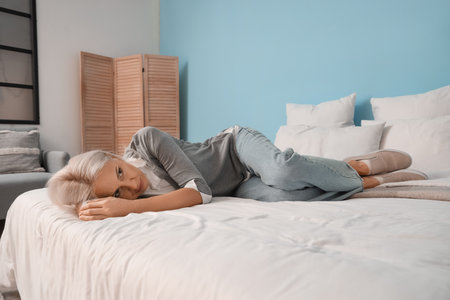 Depressed mature woman lying in bedroomの写真素材