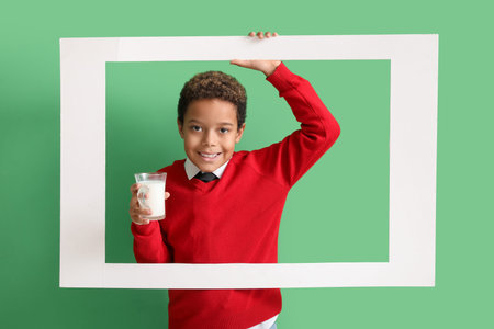 Little African-American boy with glass cup of milk and frame on green backgroundの写真素材