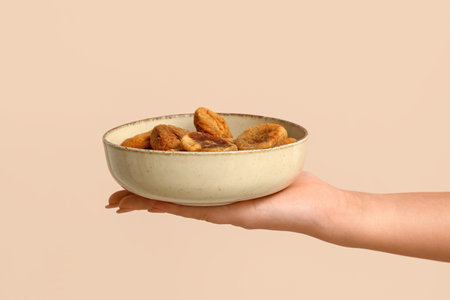 Female hand holding bowl with tasty dried figs on beige backgroundの写真素材
