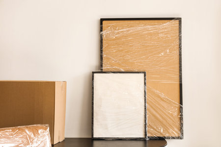 Blank frames wrapped in stretch film on table in office. Moving day concept