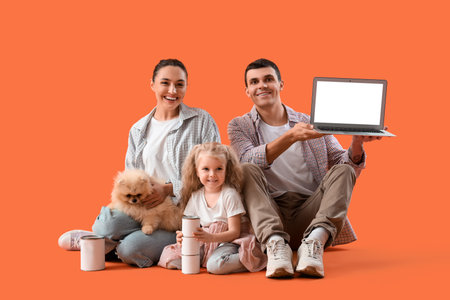 Happy family with laptop and paint cans sitting on orange backgroundの写真素材