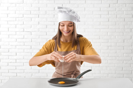 Young female chef with pan frying egg on white brick wall backgroundの写真素材
