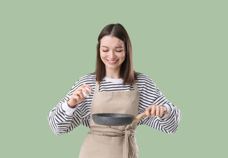 Pretty young woman in apron with chicken egg and frying pan on green backgroundの写真素材