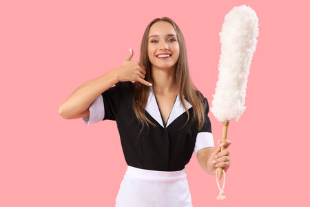 Young chambermaid with pp-duster showing call me gesture on pink background
