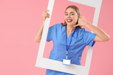 Female doctor with frame showing "call me" gesture on pink backgroundの写真素材