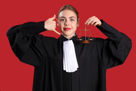 Young judge with justice scales showing "call me" gesture on red backgroundの写真素材