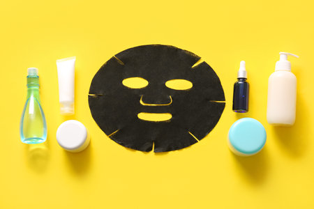 Facial sheet mask with different cosmetic products on yellow backgroundの写真素材