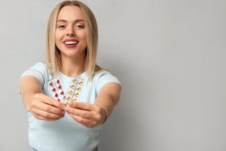Young woman with blisters of vitamin A pills on light backgroundの写真素材