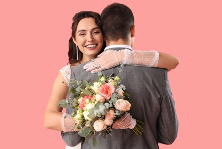 Young wedding couple with bouquet of flowers hugging on pink backgroundの写真素材