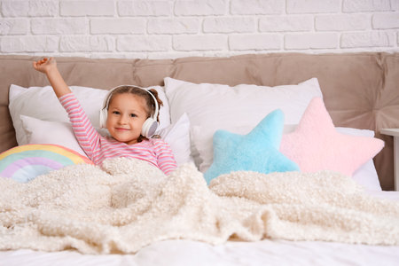 Cute little girl with headphones lying in bedroomの写真素材