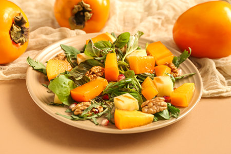 Plate of delicious salad with persimmon, walnut and pomegranate seeds on beige backgroundの写真素材