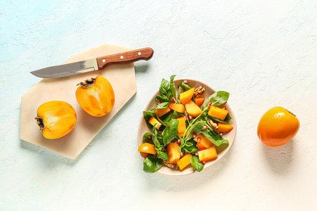 Bowl of delicious salad with persimmon, pomegranate seeds and walnut on light blue backgroundの写真素材