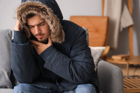 Frozen young man in puffer jacket at homeの写真素材