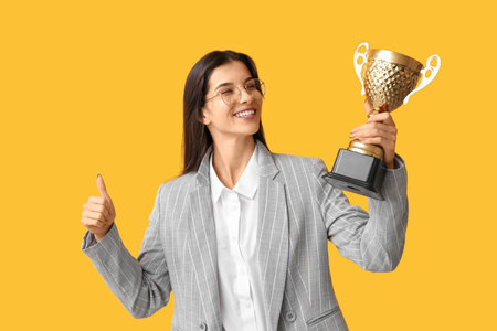 Young businesswoman with gold cup on yellow backgroundの写真素材
