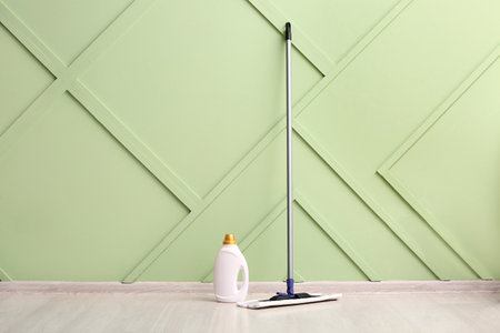 Wooden laminate floor with mop and bottle of detergent near green wallの写真素材