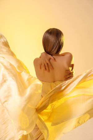 Beautiful young elegant woman with fabric on yellow background, back viewの写真素材