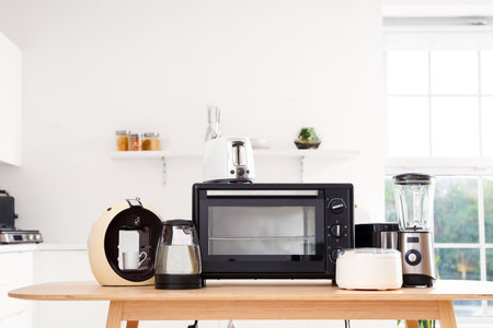 Wooden table with set of modern appliances in light kitchenの写真素材