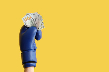Female hand in boxing glove with money on yellow backgroundの写真素材