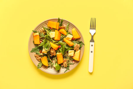 Plate of delicious salad with persimmon, pomegranate seeds and walnut on yellow backgroundの写真素材
