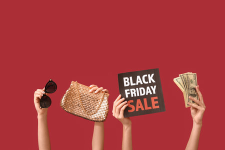 Female hands holding poster with text BLACK FRIDAY SALE, money and women accessories on red backgroundの写真素材