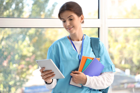 Female medical intern with tablet computer and copybooks in hallの写真素材