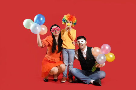 Happy family in costumes and carnival masks with balloons on red backgroundの写真素材