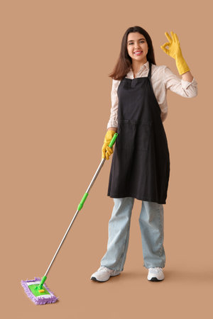 Young woman with floor mop showing OK on beige backgroundの写真素材