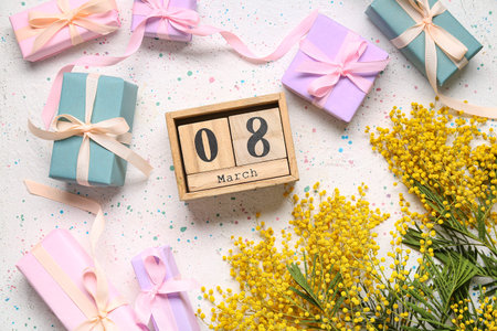 Cube calendar with date MARCH 8, gift boxes and mimosa on white spotted table. International Women's...