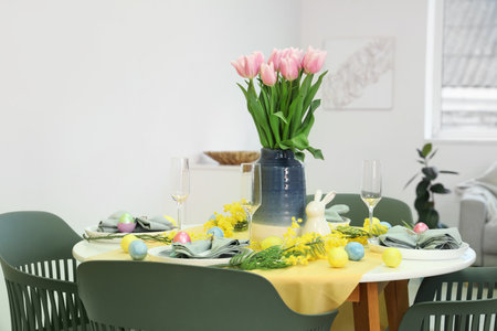 Festive Easter table setting with vase of tulips, mimosa flowers and painted eggsの写真素材