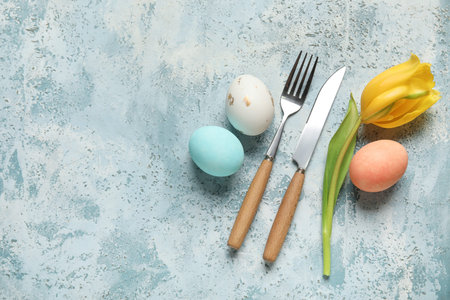 Cutlery for table setting with Easter eggs and yellow tulip on light blue background