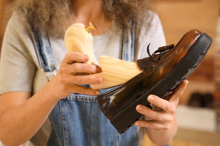 Female shoemaker with wooden shoe tree and boot in workshop, closeupの写真素材
