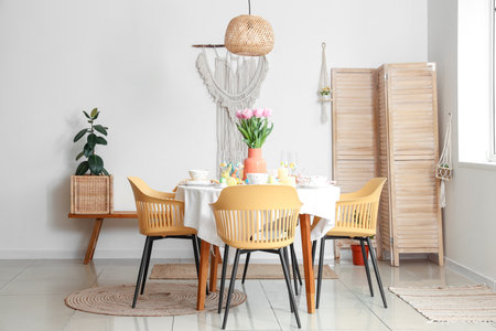 Festive table setting with vase of flowers, painted eggs and Easter bunnies in dining roomの写真素材