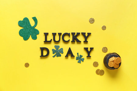 Words LUCKY DAY with clovers and pot of golden coins for St. Patrick's celebration on yellow backgroundの写真素材