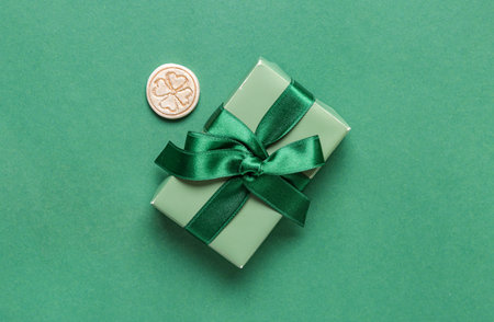 Gift box with golden coin for St. Patrick's Day celebration on green background