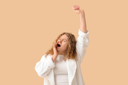 Sleepy young woman with hair scalp massager on beige backgroundの写真素材