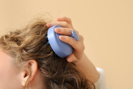 Young woman using hair scalp massager on beige background, closeupの写真素材