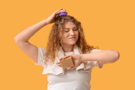 Beautiful young woman using hair scalp massager with shampoo bar on yellow backgroundの写真素材