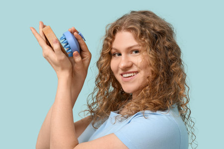 Beautiful young woman with hair scalp massager and shampoo bar on blue backgroundの写真素材